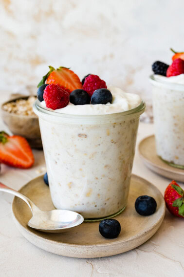 Overnight oats with yogurt in a glass cup, on a small plate, and topped with fresh berries.