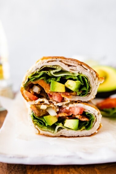 Two sections of a cottage cheese wrap with turkey, tomato, avocado, lettuce and onion visible inside the wrap.