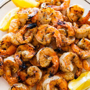 A large plate full of grilled shrimp with lemon wedges on the side.