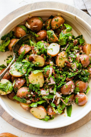 A no mayo potato salad in a large bowl with potatoes, spinach, sun dried tomatoes and fresh herbs.