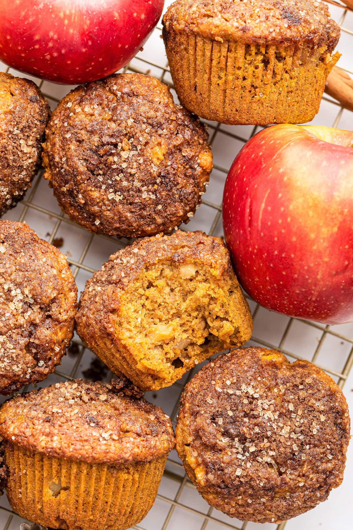 Multiple apple muffins on a cooling rack with one muffin having a bite taken from it.