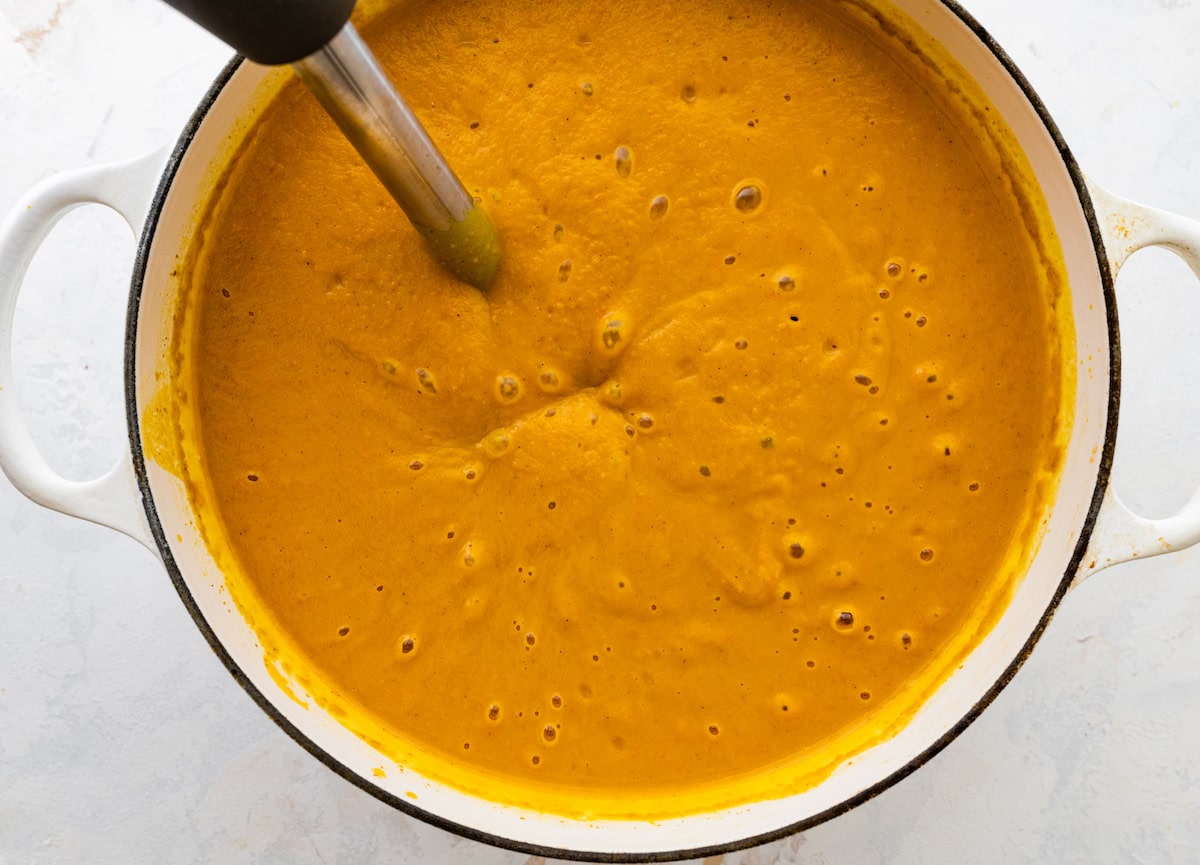 An immersion blender blending all ingredients for an autumn soup in a large pot.