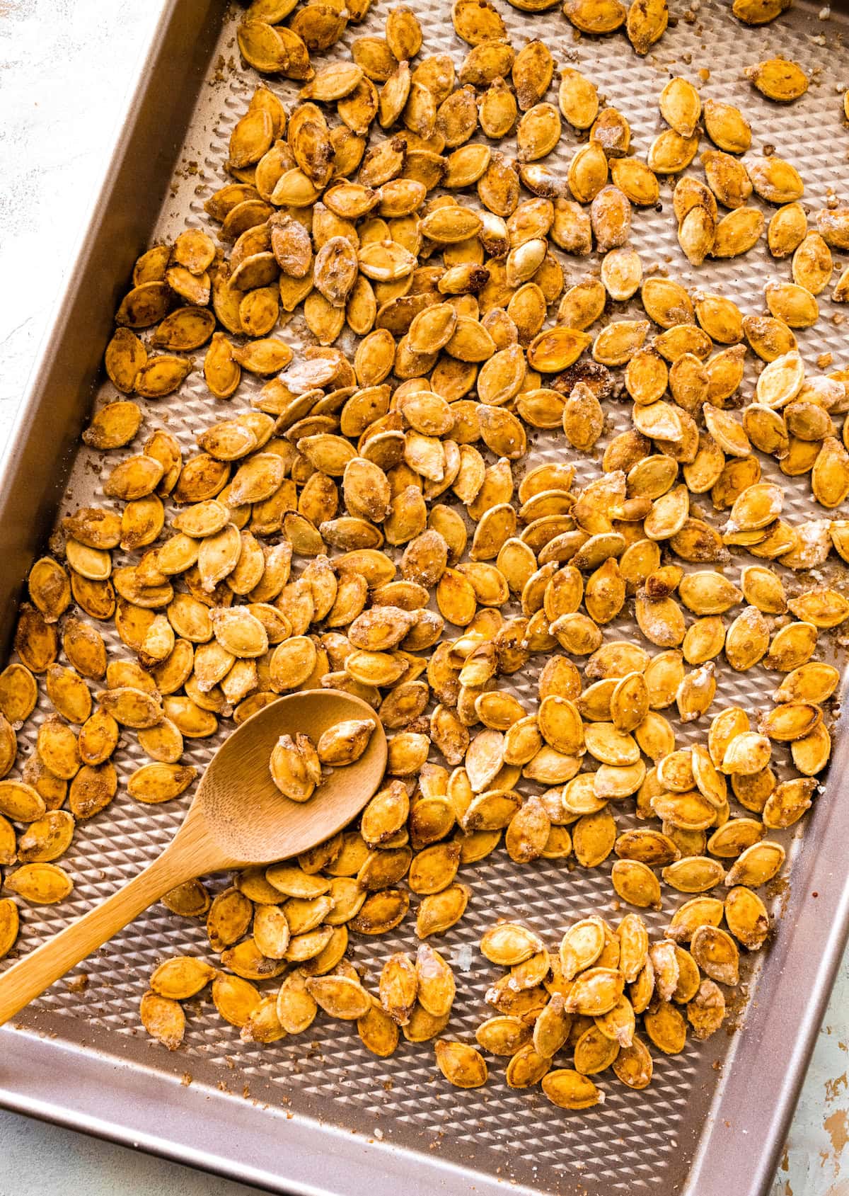 Roasted and salted pumpkin seeds on a baking tray with a wooden spoon.
