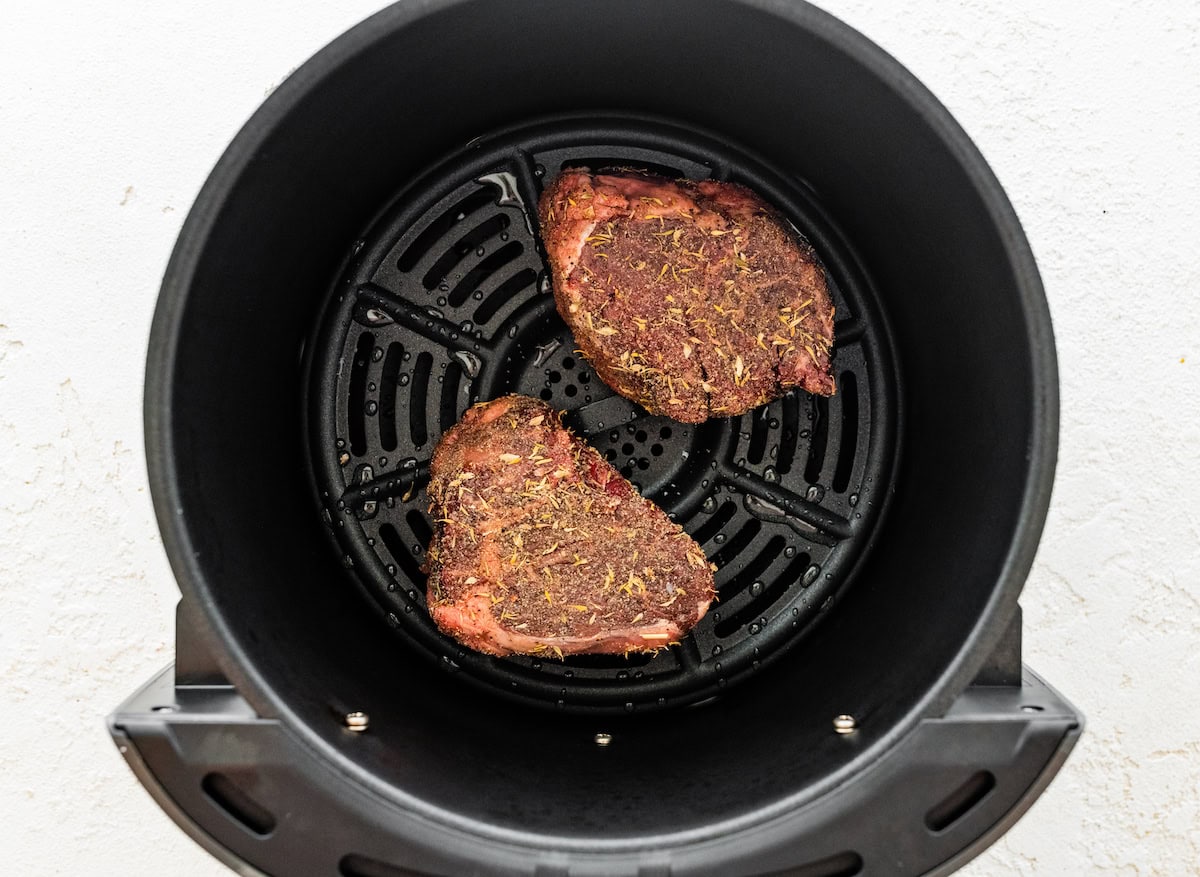 Two uncooked filet mignon pieces in the basket of an air fryer.