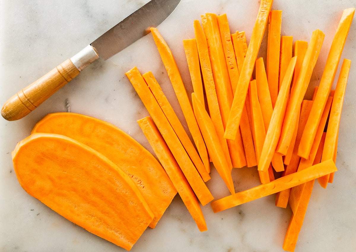 A sweet potato cut into fries on a cutting board. The fries are next to a small knife.