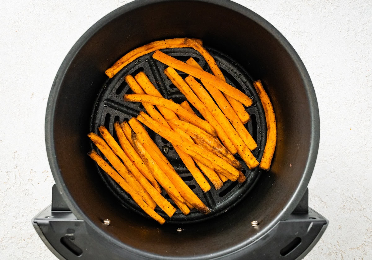 Sweet potato fries in the basket of an air fryer after being cooked.