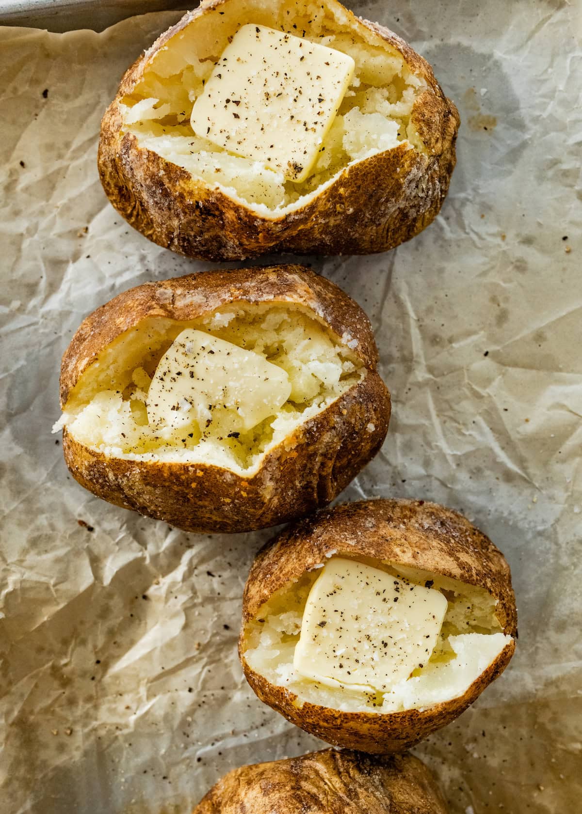 Baked potatoes split open on a baking tray with butter and seasonings.