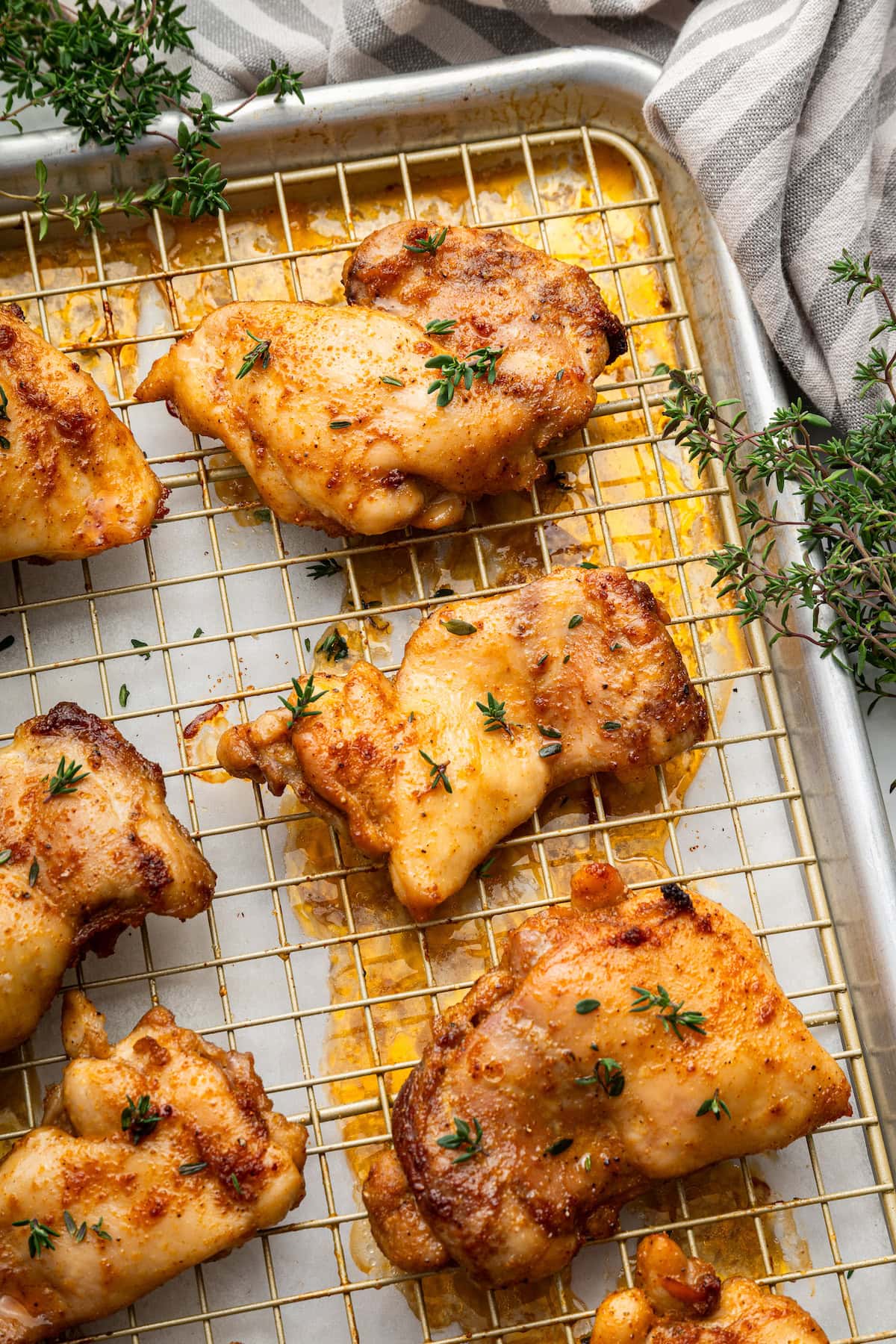 Baked boneless chicken thighs garnished with fresh herbs on a metal cooling rack that is on a baking tray.