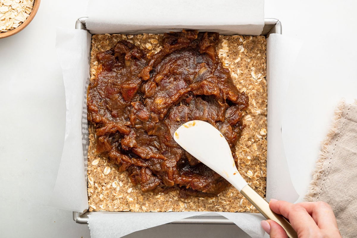 Date paste being spread over a oat base in a square pan.