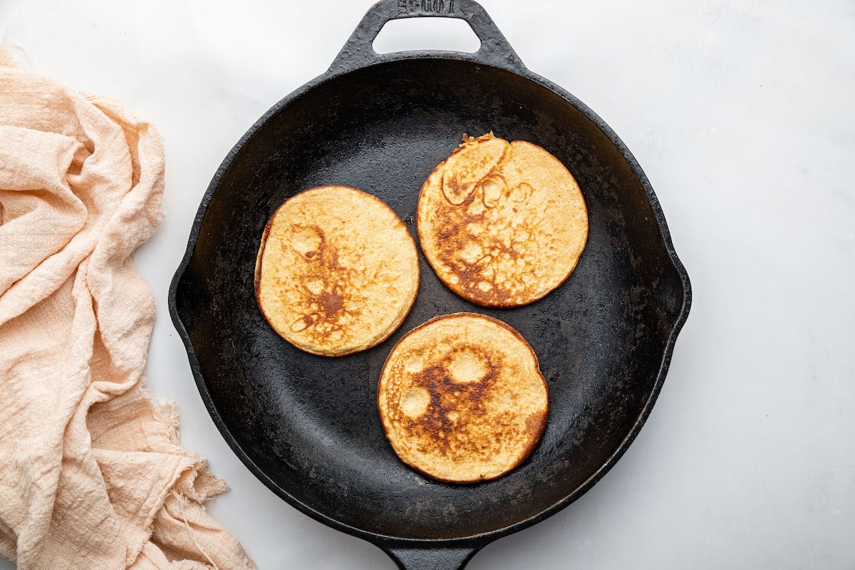 Three small greek yogurt pancakes cooking on a skillet.
