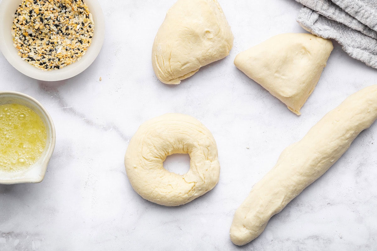 Dough used for protein bagels separated into four portions. One of them is formed into a bagel shape.