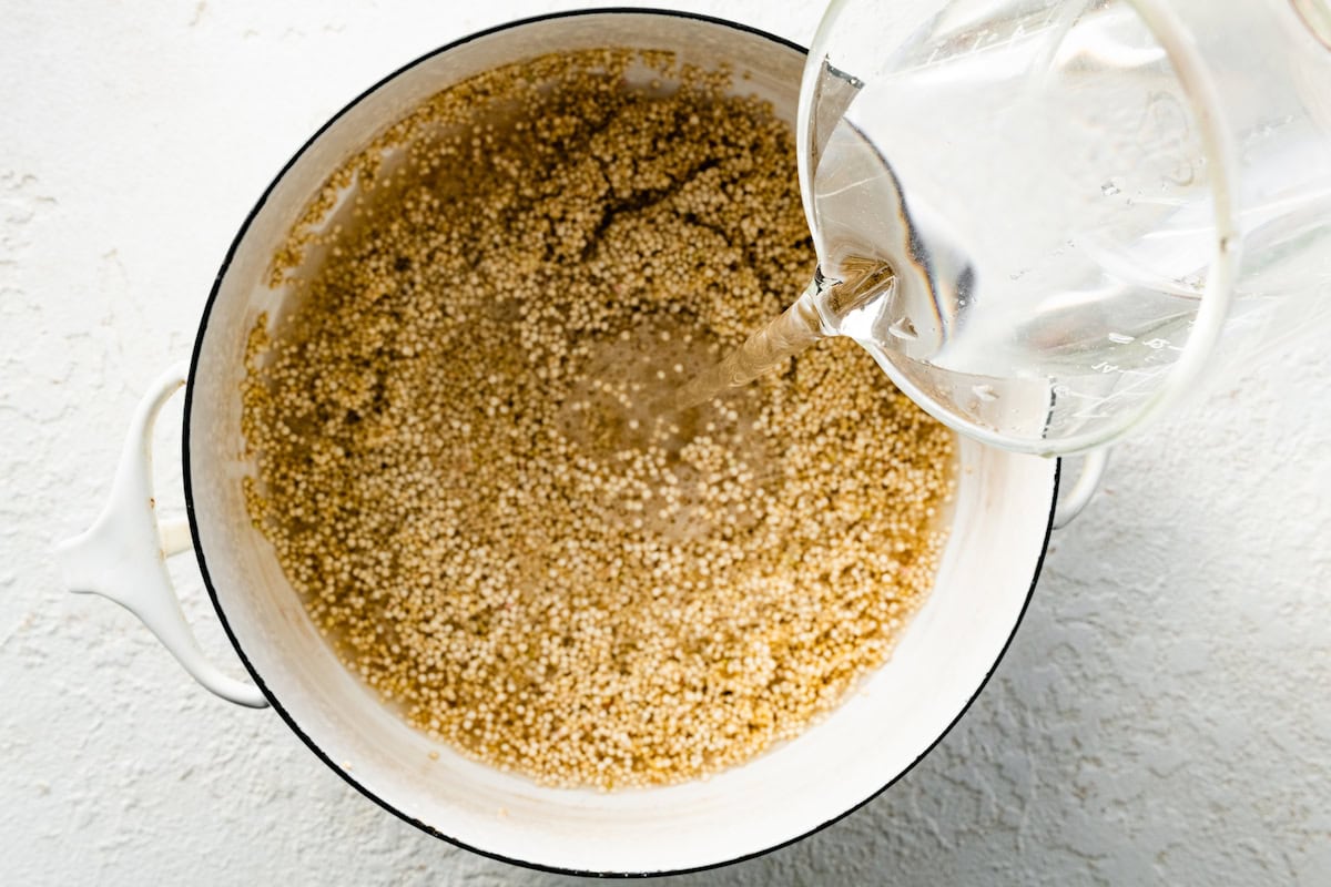 Water being poured into a large white pot of uncooked quinoa.